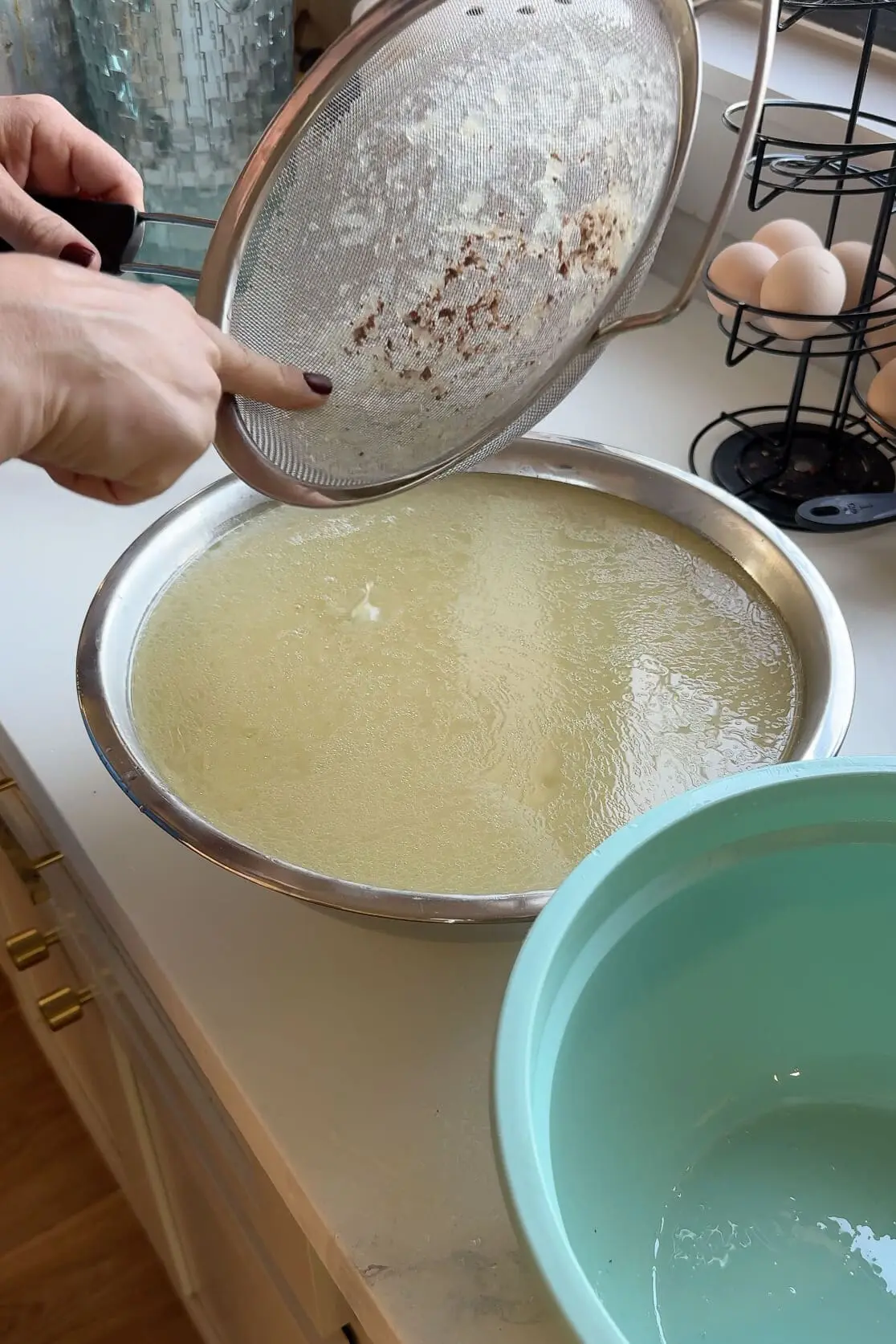 Straining homemade chicken stock through a fine mesh strainer to achieve a smooth, clear, and golden broth.